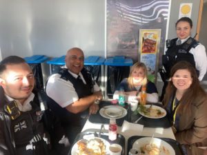 Four police officers and a civilian sit around a table with their lunch, smiling for the photo.